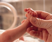 small premature baby lies in an incubator a grown hand reaches in grasping the foot in caring manner